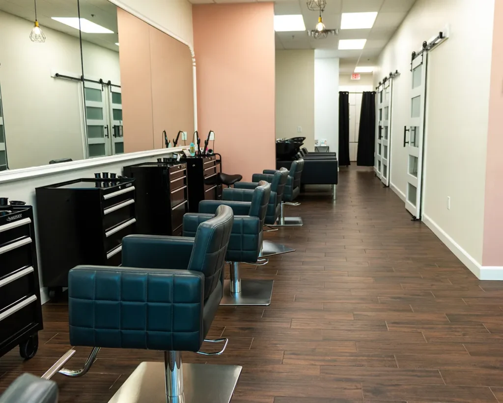 Empty modern hair salon with black styling chairs, mirrors, and tool carts lined up along a wall with wooden floors and overhead lighting. - Salon Blissful, Mesa and Peoria, AZ